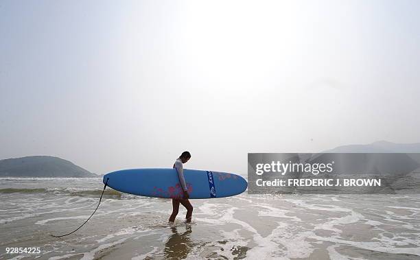 To go with AFP story by Dan Martin: LIFESTYLE-CHINA-LEISURE-SURFING A surfer carries her board to ride a wave in the waters of the South China Sea at...