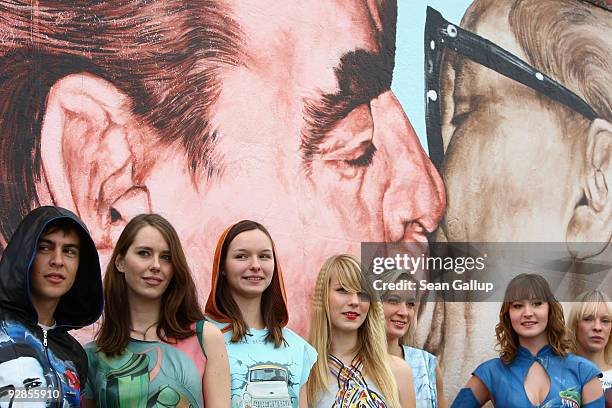 Models wearing clothes inspired by murals on a portion of the remaining Berlin Wall known as the East Side Gallery pose next to the "Brotherkiss"...