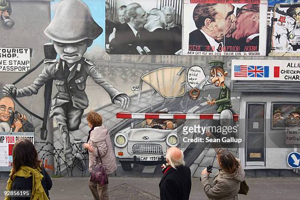 Visitors walk by a mural on a souvenir shop at a still-existing portion of the former Berlin Wall known as the East Side Gallery on its official...
