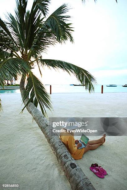 Woman sitting on Villingili beach, working with a notebook and mobile phone, surfing the internet. The island is owned by the luxurious Shangri-La's...