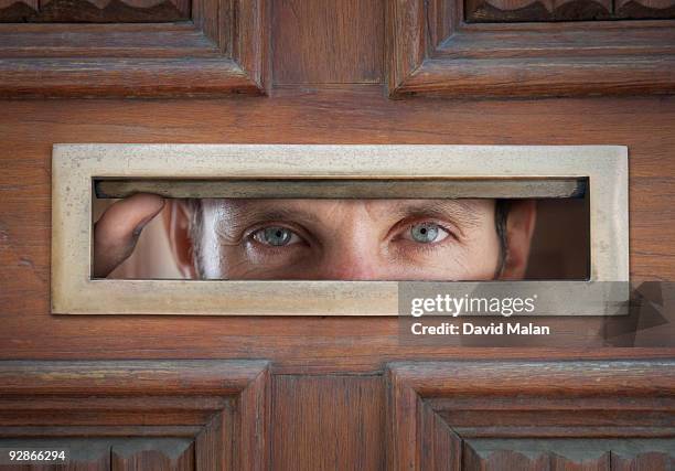 man peeping through letterbox in door - ranura de buzón fotografías e imágenes de stock