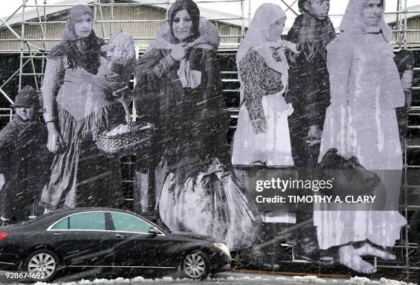 Taxi passes a new exhibit by French Street artist JR in a snowstorm outside the show during the press preview at the Armory Show March 7, 2018 at...