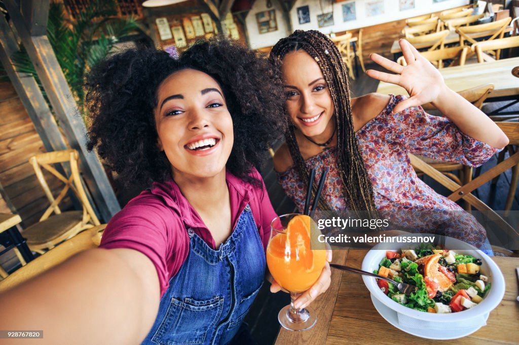 Unga kvinnor i restaurang dricka saft och äta sallad