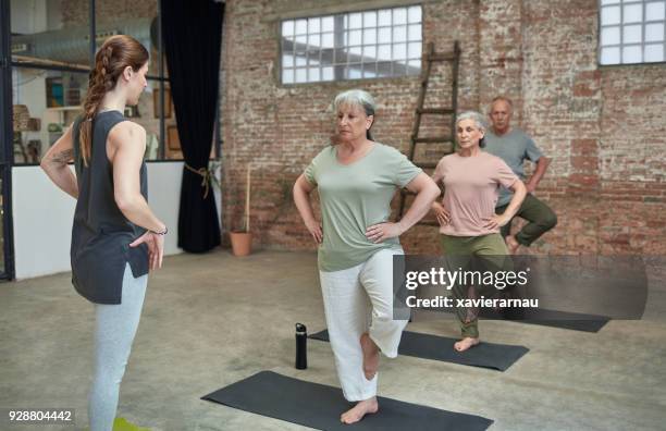 female coach teaching yoga to seniors at gym - senior standing on one leg stock pictures, royalty-free photos & images