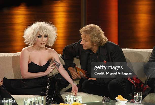 Singer Lady Gaga sits next to host Thomas Gottschalk during the 'Wetten dass...?' show at the Volkswagenhalle and shows off her tattoo of a Rilke...