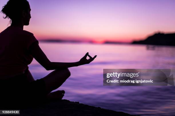 young woman meditating by peaceful sea - purple sunset stock pictures, royalty-free photos & images