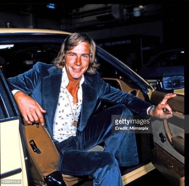 James Hunt, smiles to camera, whilst sitting in the front seat of his car. James is wearing a medallion, white patterned shirt and blue velvet suit,...