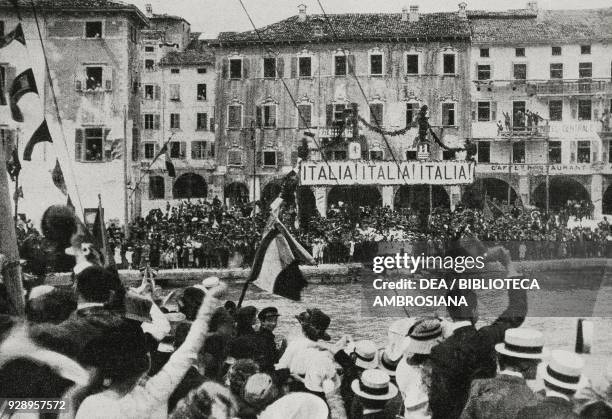 On Statute day, a cheering crowd welcomes the first Italian boat arriving in Riva di Trento, Italy, after the liberation of the city, photo by...