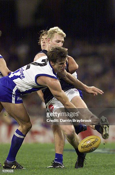 Leigh Colbert for the Kangaroo's, attempts to stop Scott Freeborn for Carlton, kicking to a team mate, in the match between the Kangaroos and the...