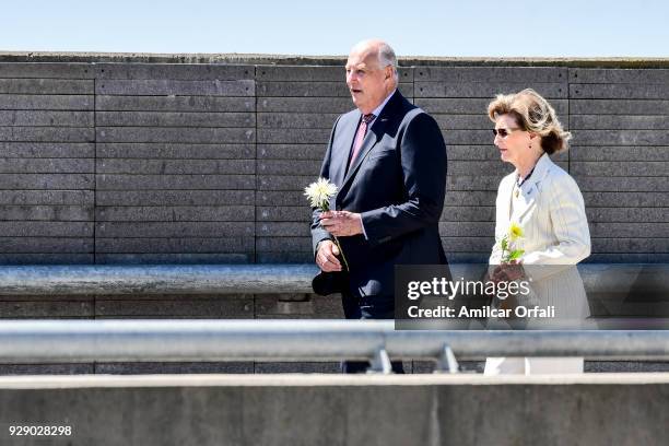 King Harald V of Norway and Queen Sonja of Norway hold flowers and walk next to a wall with the names of the victims of Argentina's dictatorship...