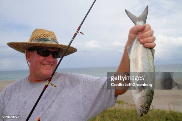 Fisherman holding a bluefish that he has caught on Juno Beach.