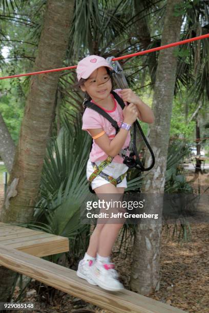 An Asian girl walking on an aerial treetop tree canopy rope bridge at ZOOm Air Adventure Park.