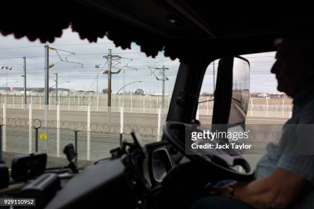 Barbed wire fencing is seen through the window as lorry driver Bob Evans sits waiting to board a freight train in Calais on March 6, 2018 in Calais,...