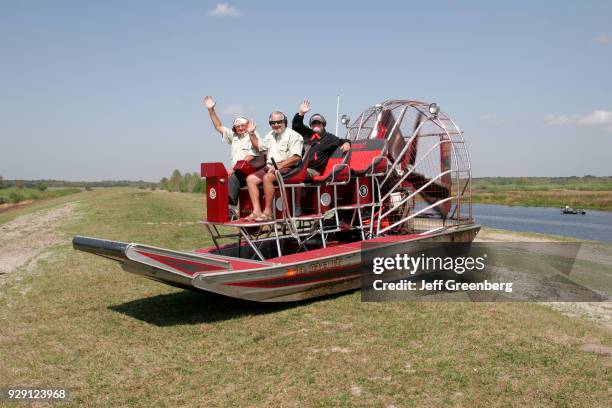 Two men and a woman sat on an airboat on dry land at Camp Mack River Resort.