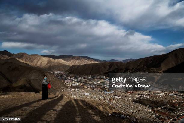Tibetan Buddhist woman pauses while walking the kore and stands on a hill overlooking the Labrang Monastery during Monlam or the Great Prayer, on...