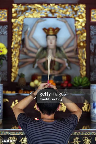 Thian Hock Keng Temple. A Chinese young man praying and offering incense. Buddhist Worshipper. Burning incense sticks. Man praying. Singapore.