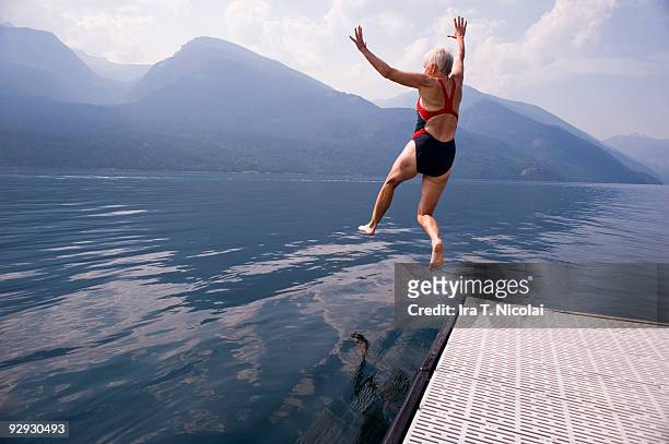 female babyboomer jumping into lake - freiheit stock-fotos und bilder