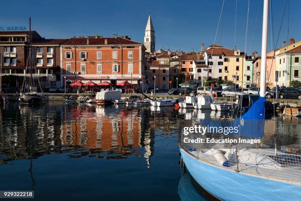 Marina at old fishing town of Izola Slovenia on the Adriatic coast with Parish Church of St Maurus tower and colorful reflected buildings.