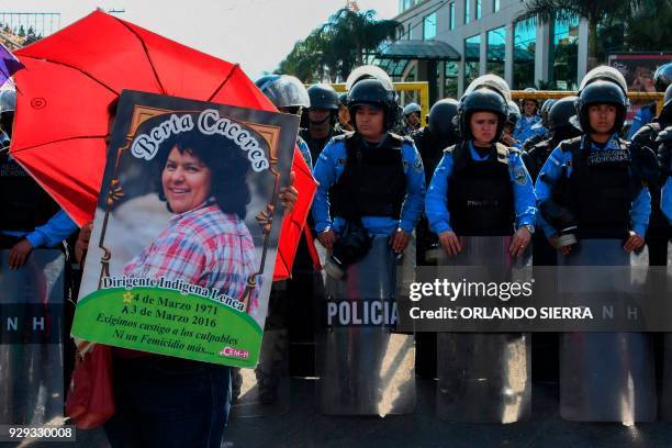 Riot police officers stand guard, as a woman holds a banner depicting slain Honduran activist Berta Caceres during a demonstration in demand of...