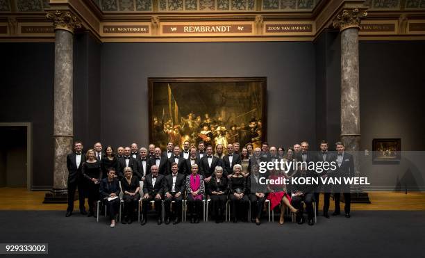 Guests pose for a photo during a special dinner for the Masters of the World, former skating champions, in front of a poster of "the Night Watch"...