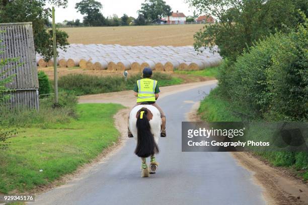Woman riding a horse down quiet country lane, Bromeswell, Suffolk, England, UK.