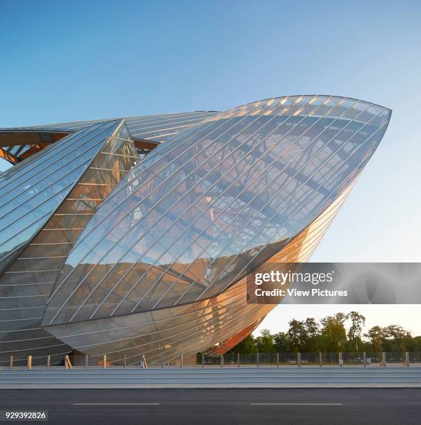 Fondation Louis Vuitton, Paris, France. Architect: Gehry Partners LLP, 2014. Partial glass sail facade against Bois de Boulogne in morning light.