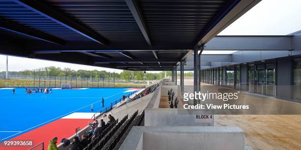 Hockey field in blue with canopied spectator stand. Eton Manor - Lee Valley Hockey and Tennis Centre, London, United Kingdom. Architect: Stanton...