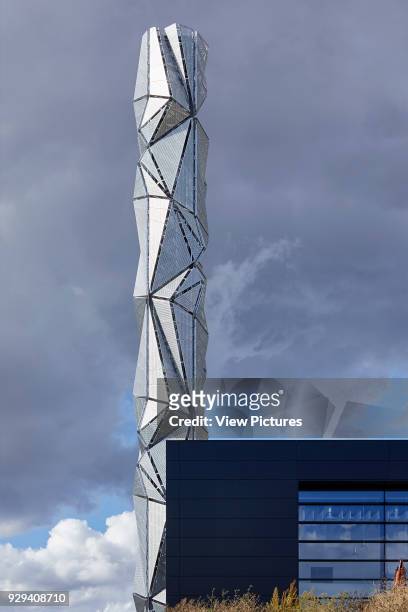 View of the energy centre and sculptural chimney with heavy cloud. Greenwich Energy Centre / The Optic Cloak, Greenwich, United Kingdom. Architect:...