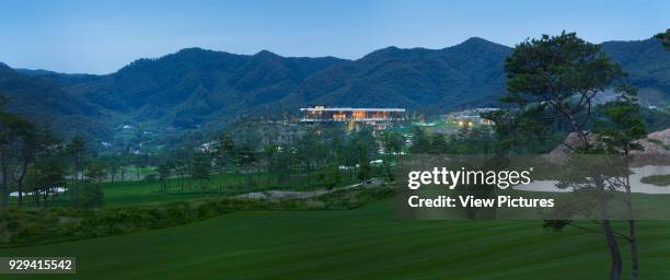 Whistling Rock Golf Clubhouse, Chuncheon, Korea, South. Architect: Mecanoo, 2012. Distant panoramic view across golf course towards clubhouse at dusk.