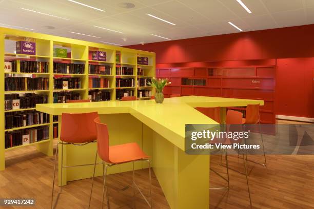 Yellow star-shaped table with orange chairs and yellow tables against red wall on forst floor.