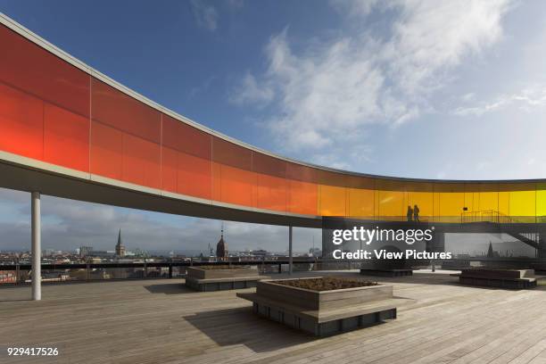 Your Rainbow Panorama' circular aerial walkway with cityscape beyond and timber-floored rooftop terrace and silhouetted figures. ARoS Aarhus...