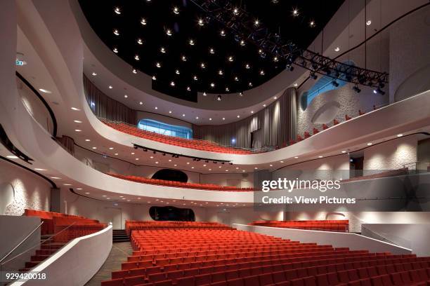 Main hall, with red seating against curving white walls and balconies. Musikkens Hus Aalborg, Aalborg, Denmark. Architect: Coop Himmelbau, 2014.