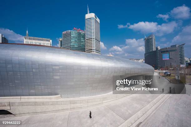 Dongdaemun Design Plaza , Seoul, Korea, South. Architect: Zaha Hadid Architects, 2014. Lateral view of building and concrete promenade with high rise...