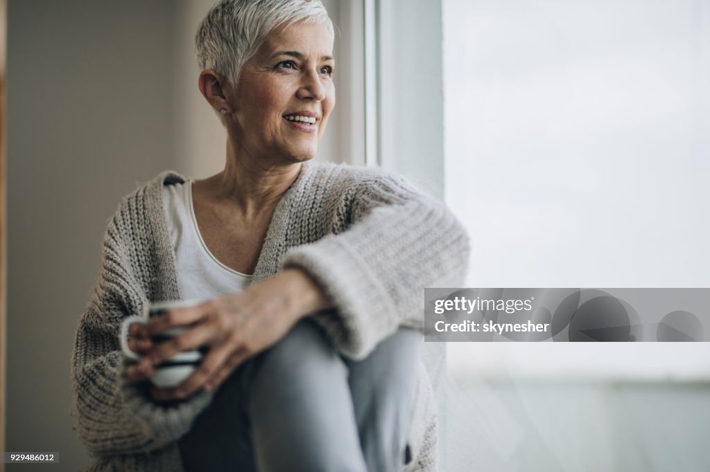 Happy mature woman relaxing by the window during coffee time.