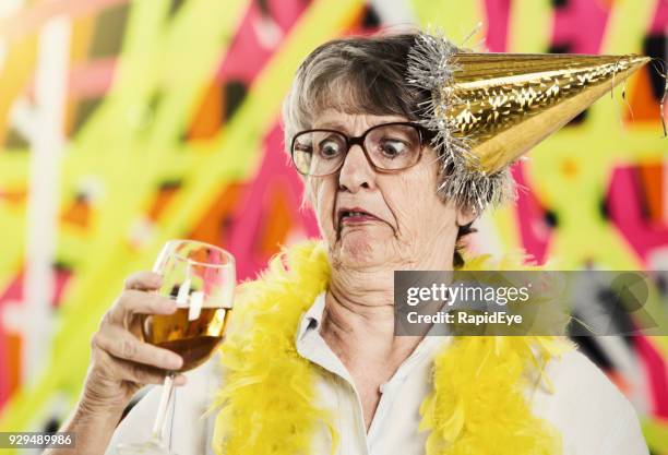 old woman in party hat looks at wine glass, horrified - senior women wine stock pictures, royalty-free photos & images