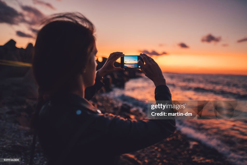 Frau am Strand den Sonnenuntergang fotografieren
