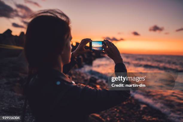 frau am strand den sonnenuntergang fotografieren - smartphone strand stock-fotos und bilder