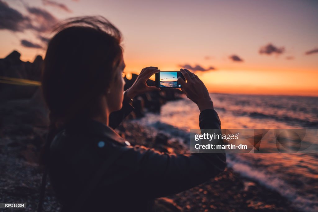 Woman at the beach photographing the sunset