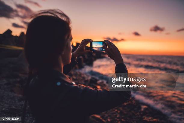 woman at the beach photographing the sunset - máquina fotográfica imagens e fotografias de stock