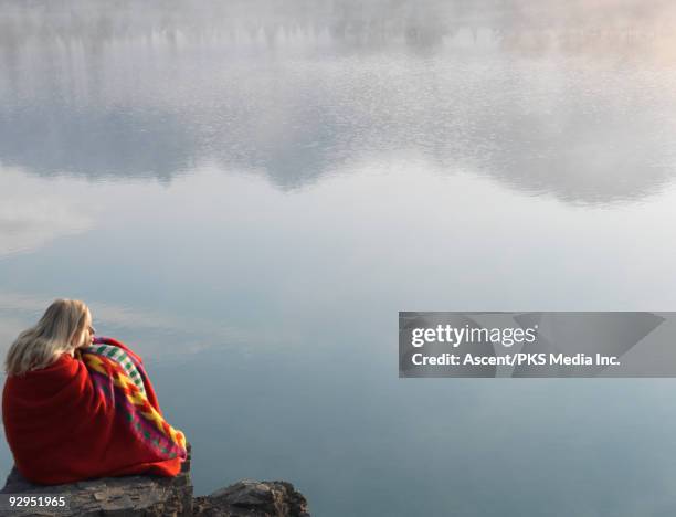 woman nestles under blanket at lake edge, sunrise - nestles stock pictures, royalty-free photos & images