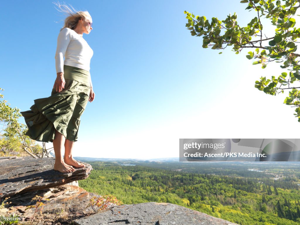 Woman stands on rock overlooking forest, windy day