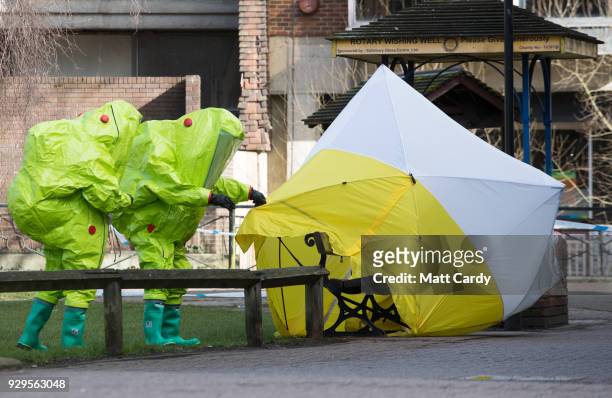 Specialist officers in protective suits secure the police forensic tent that had been blown over by the wind and is covering the bench where Sergei...