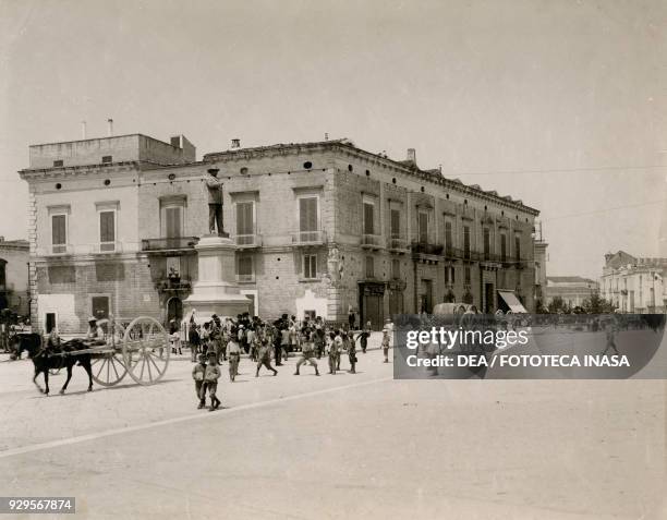 Statue of Matteo Renato Imbriani in Piazza Plebiscito, with the Gioia palace, children and carts with horses in the background, Corato, Apulia,...