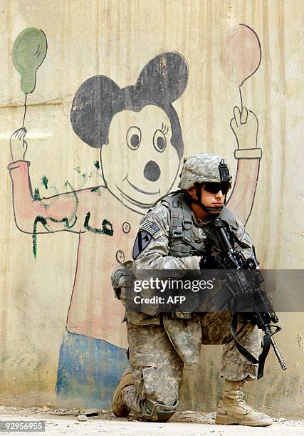 Army soldier from 3rd Battalion 8th Cavalry Division kneels in front of an image of Mickey Mouse painted on a wall while on patrol in the northern...