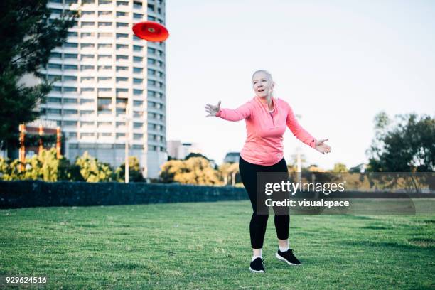 active senior lady throwing frisbee - throwing frisbee stock pictures, royalty-free photos & images