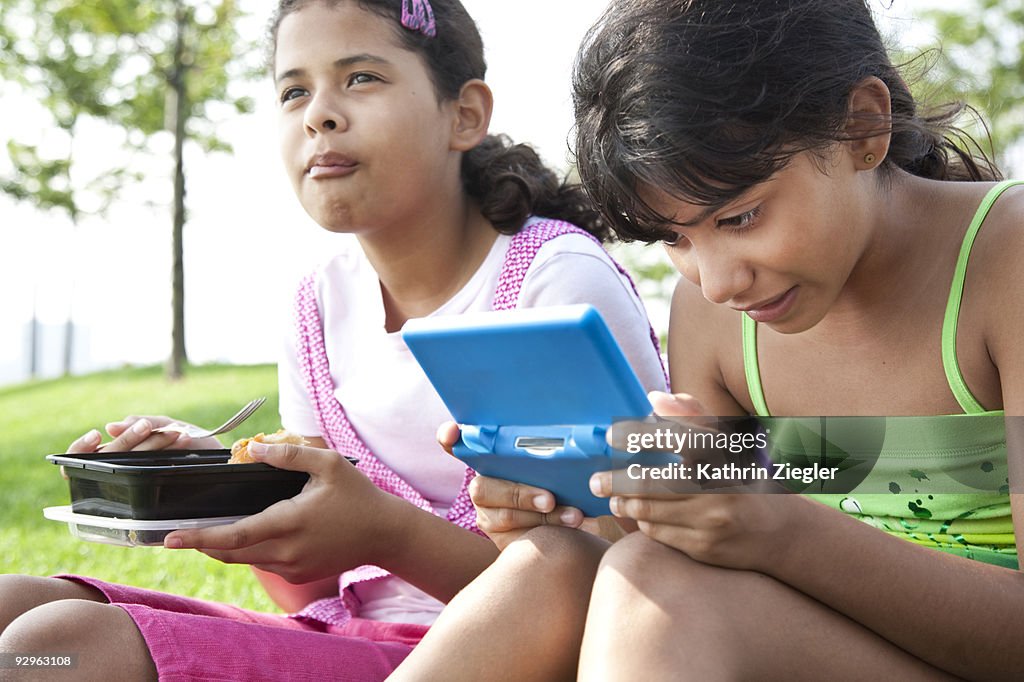 Two young girls eating, playing electronic games