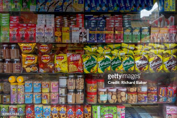 Detail of assorted snacks including biscuits, crisps and other merchandise on shelves in a corner shop window on Gerrard Street, Chinatown, on 5th...