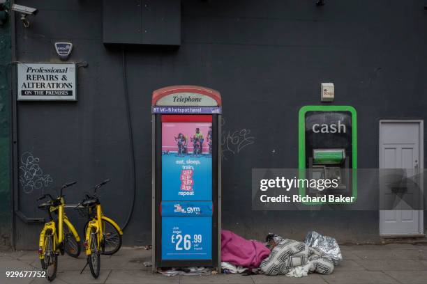 The sleeping bag of a homeless person inside a phone kiosk and next to an ATM cash dispenser operated by Bank Machine on Old Street, aka Silicon...