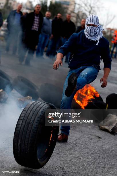 Palestinian demonstrator kicks a burning tire during clashes with Israeli security forces following a demonstration in the West Bank city of Ramallah...