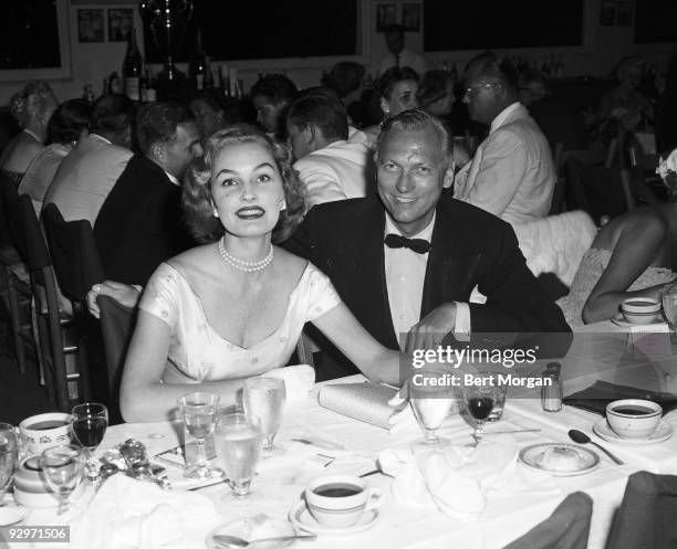 Earl Blackwell and Pamela Curran seated and smiling at a banquet at the Palm Beach Polo Club, Palm Beach, Florida, c1955